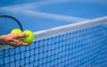 Old asian man hold two tennis balls in right hand, selective focus, blurred racket, net and blue tennis court as background Royalty Free Stock Photo